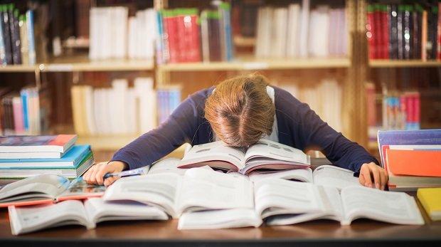 Studentin über einer Vielzahl an Büchern am Schreibtisch eingeschlafen