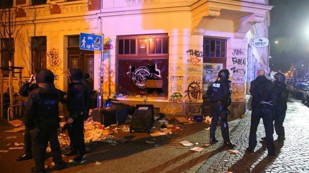 Polizisten stehen am 11.01.2016 im Stadtteil Connewitz in Leipzig (Sachsen) vor zerbrochenen Fensterscheiben und verwüsteten Müllcontainern.