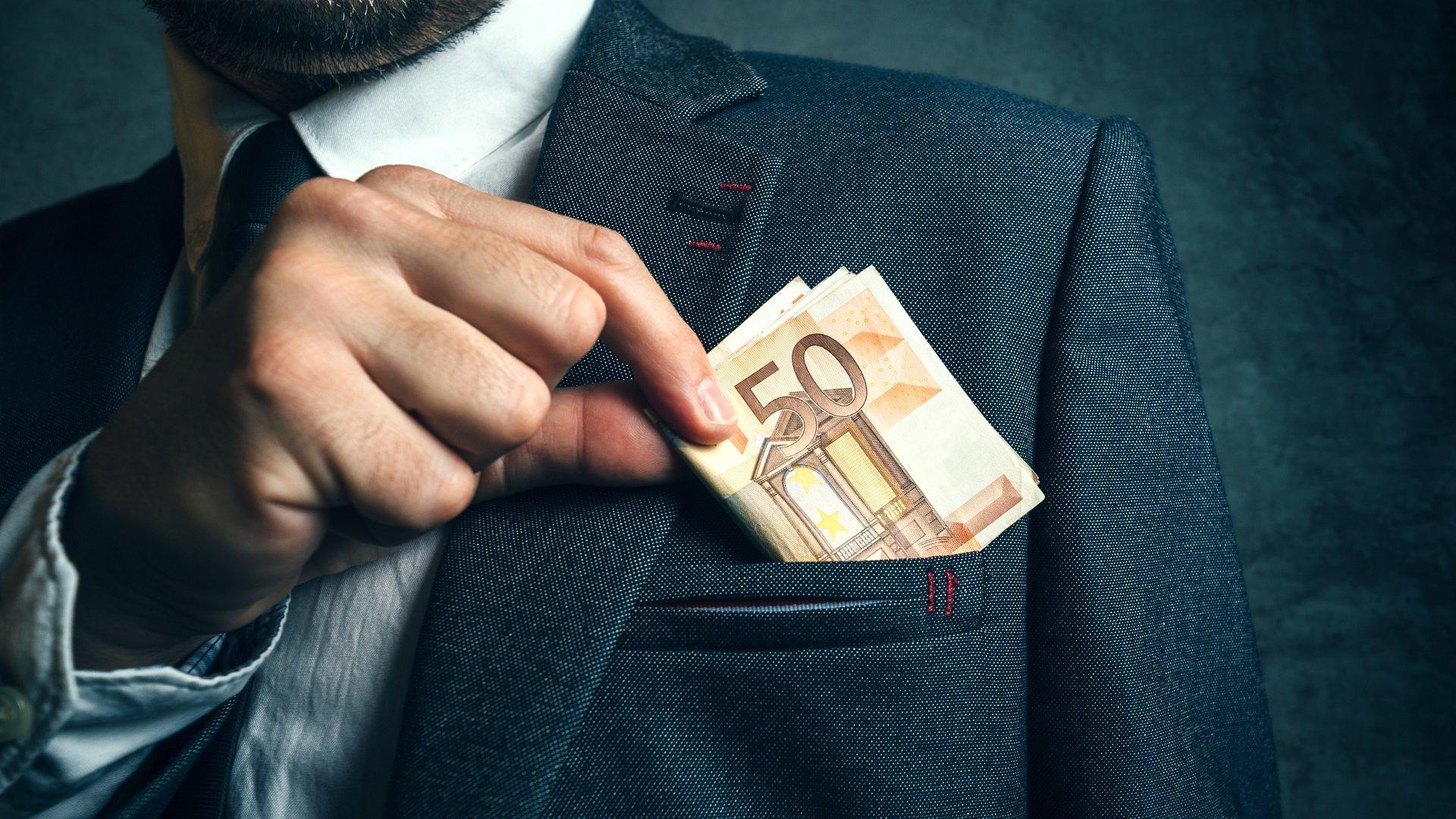 Ein Mann steckt sich Geld in die Tasche seines Anzugs (Symbolbild)